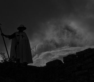 A medieval guard sillhouetted against a dark sky