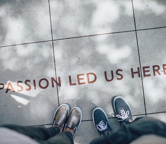 The feet of 2 persons standing on a ground with the expression “Passion led us here”
