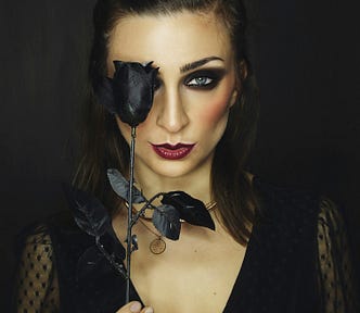 Fancy woman in a black dress holding up a black rose in front of one eye