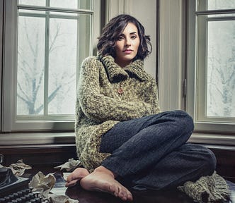 A woman sitting on a desk looking thoughtful.