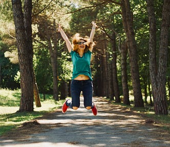 woman on a walking path jumping in the air with knees bent and hands in the air