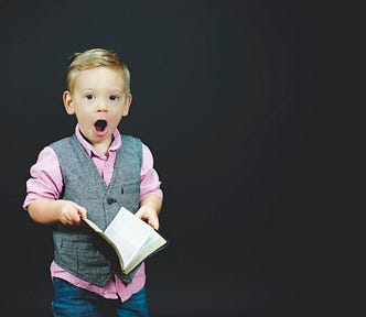 Young boy holding an open book making a surprised oh-face. Adam Murauskas. Fix Your Picker.com. Relationship Coach. Attachment Style.