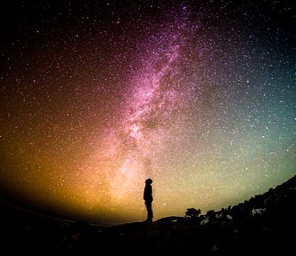 The dark image of a man staring up at a beautiful night sky filled with stars.
