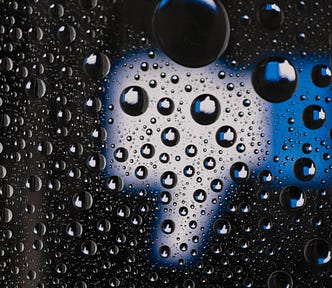 Facebook like icon “thumbs up” turned upside down on a black background with water drops