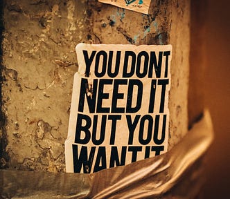 A poster on a crumbling wall with the text ‘You don’t need it, but you want it’.