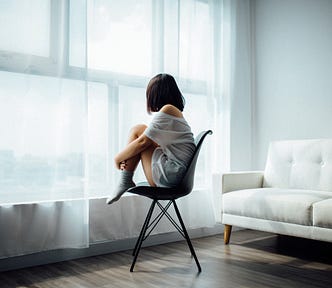 A woman sitting in a chair by the window watching and reflecting.