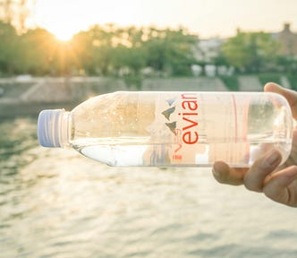 A bottle of Evian mineral water in a person’s hand. There is a lake in the background
