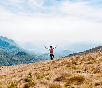 Person with both arms raised looks out into a foggy mountain range