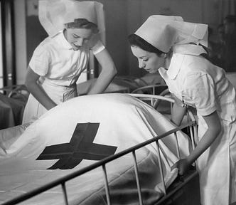 Vintage black and white photograph of two female nurses caring for a patient in bed.