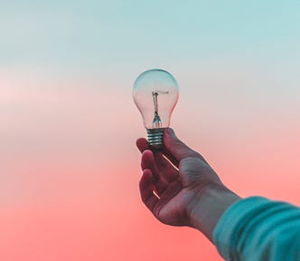 A person holding up a lightbulb on a gradient background.