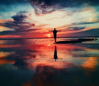 person standing in a reflective sunset sky