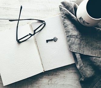 an open blank notebook with eyeglasses, a key, and a cup of coffee on the side