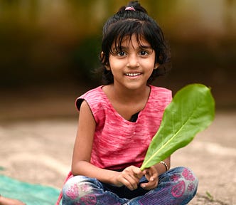 Little Indian girl sitting crosslegged holding a leaf