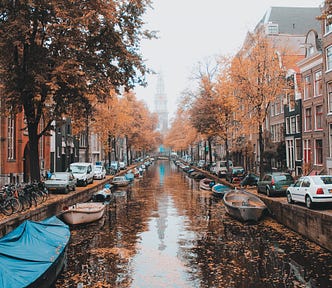 Amsterdam canals in autumn with orange and brown leaves on the trees and floating on the canal alongside small boats.