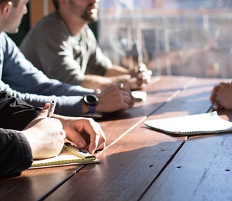 people sitting on chair in front of table while holding pens during daytime