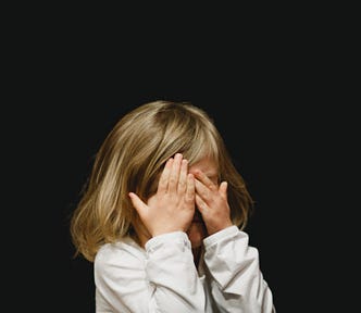 Young girl with blonde hairs and white longsleeve holding her hands in front of her eyes