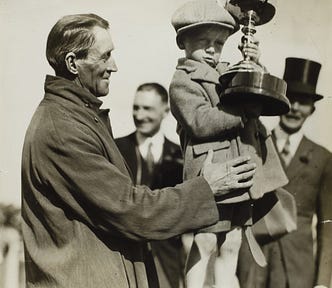 Man holding up a child who is holding an enormous trophy.