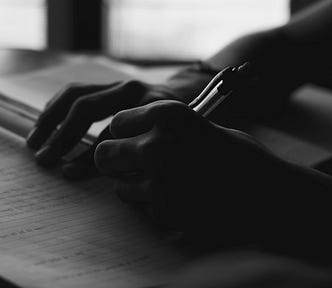 a black and white image of a person’s hands as they write in a notebook