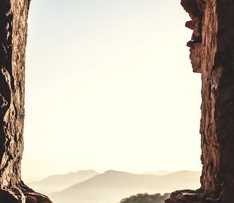 A bird sits at the entrance to a cave while the sun rises.