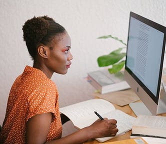 Black woman making notes while studying at a computer