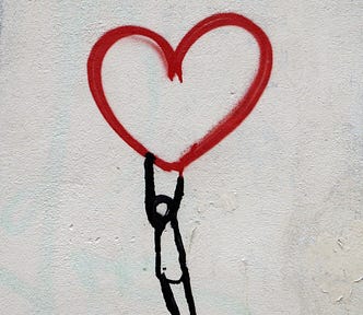 A stick figure holding on to the bottom of a red heart.
