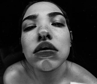 A young woman with freckles looking into the camera at an odd angle, distorting her features and giving a slightly weird vibe.