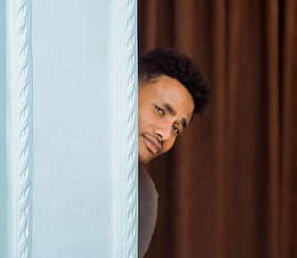 A man with an inquisitive look peaking behind a wall.