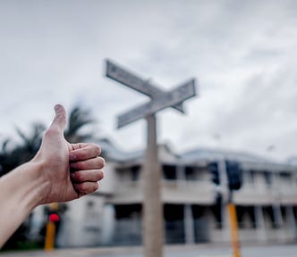 Hitchhiker’s thumb extended on a street corner near a set of street signs