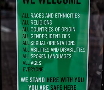 Green sign with white text. We welcome all races, all religions, all gender identities, all ages, etc. Women in Tech. Diversity. Business. Technology