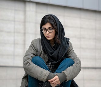 Brunette, Muslim female wearing dark grey hijab sitting cross-legged.