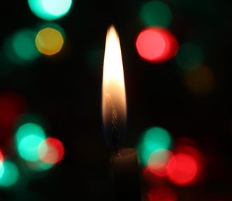 Black background with brilliant green and red lights and a single candle flame in the center