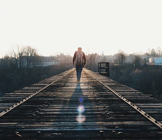 backlit man walking down train tracks alone