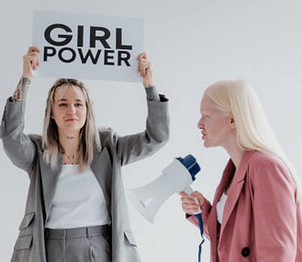 a woman in gray holding a sign and a woman in pink using a megaphone