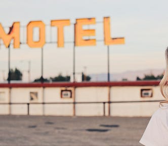 An old motel sign with a young, long-haired, beautiful woman standing to the right of it