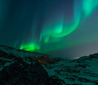a green aurora with many folds, hanging in a dark sky above dark mountains