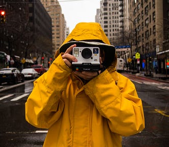 Person in yellow raincoat with a polaroid camera.