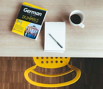 A language learning book on a desk with an empty pad of paper and coffee.