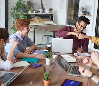 A happy team of young professionals in casual dress working in an office and having a meeting around a table, with two people fist bumping