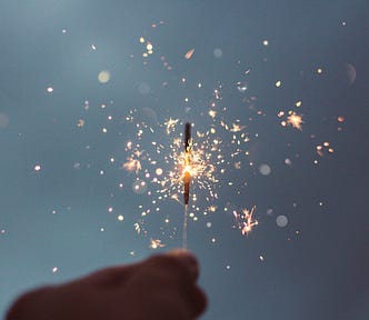 shadow of a hand holding up a sparkler against a dark grey or indigo sky