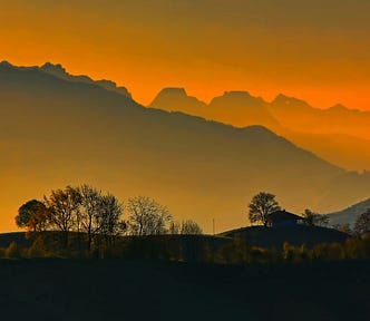 Orange-golden sunrise over a mountain range, with brushy trees silhouetted in the mist.