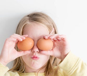 A young girl holding fresh eggs over her eyes — Not unlike my first baking experience!