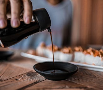 close up on a person pouring soy sauce into a small bowl in front of a platter with sushi