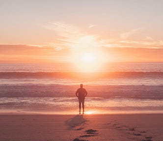 A calm person stands on the beach looking out to sea