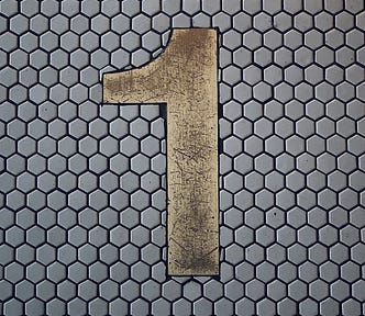 A huge metal numeral ‘one’ overlaid onto hexagonal greyish-lavender tile, alluding to the one question word in this article.