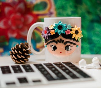 A computer next to a pinecone and a mug with a face and flowers on it