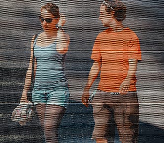 Young woman wearing shots and a summer top walking alongside a young guy in an orange tee shirt and shorts but the image is full of tiny holes, like they’re not real