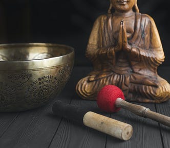 A metal singing bowl and meditating figurine.