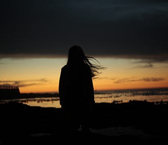 Silhouette of a person in low light looking out over the ocean