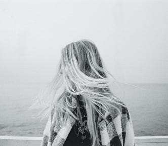 A black and white image of a woman facing the ocean with wind in her hair