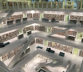 A library with five levels connected by white staircases. Blue couches are on each level, some have readers sitting on them with a book. Bookcases are white filled with rows and rows of books.